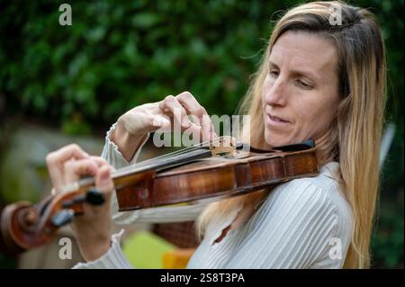 Eine fokussierte Frau spielt anmutig Geige in einer ruhigen Umgebung im Freien, ihre Hände sanft auf dem Instrument positioniert. Stockfoto