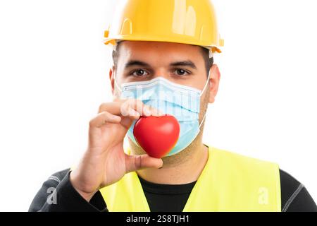 Nahaufnahme eines männlichen Konstrukteurs in Schutzkleidung mit rotem Herz tragender medizinischer Maske als Pflegekonzept isoliert auf weißem Atelierhintergrund Stockfoto