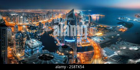 Blick auf die Skyline von Dubai bei Nacht von oben. Mit orange leuchtendem Verkehr auf den Straßen und dunkelblauem Wasser, das mit dem Himmel verschmilzt Stockfoto