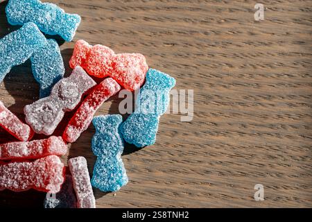 Eine bunte Auswahl an zuckerbeschichteten Gummibonbons in Rot-, Blau- und Violetttönen, die auf einer Holzoberfläche verstreut sind. Stockfoto