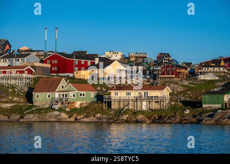 Lebendige Häuser säumen die Küste von Ilulissat und reflektieren das Sommerlicht vor einer idyllischen Kulisse der grönländischen Landschaft. Stockfoto