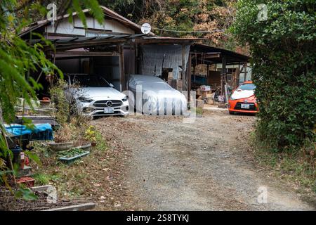 Kyoto, Japan - 27. Dezember 2024: Verlassener Parkplatz mit einem überdachten Fahrzeug und zwei geparkten Autos in ruhiger ländlicher Umgebung Stockfoto