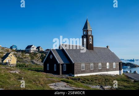 Zion's Church in Ilulissat bietet einen Einblick in grönländische Architektur und natürliche Schönheit, umgeben von farbenfrohen Häusern und dramatischen Landschaften. Stockfoto