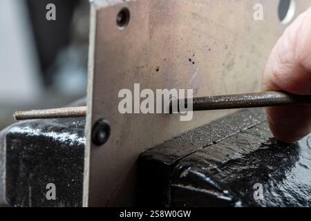 Der Handwerker arbeitet an einem kleinen Stück Metall mit runder Metallfeile, die im Schraubstock auf dem Werkstatttisch in der Garage gefasst wird, machen Sie es selbst Konzept, Nahaufnahme Stockfoto