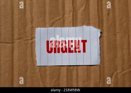 Dringende Nachricht geschrieben auf zerrissenem Papierstück mit Papppapierhintergrund. Konzeptionelles dringendes Wortsymbol. Kopierbereich. Stockfoto