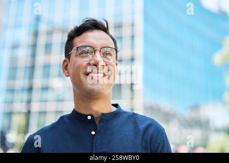 Glücklicher junger hispanischer Geschäftsmann, der wegblickt, in der Stadt stehend, Porträt. Stockfoto