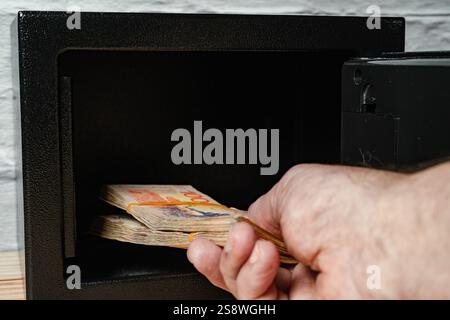 Mann, der Bargeld aus einem offenen Safe nimmt. Stockfoto