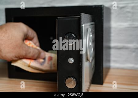 Mann, der Bargeld aus einem offenen Safe nimmt. Stockfoto
