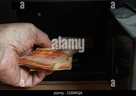 Mann, der Bargeld aus einem offenen Safe nimmt. Stockfoto