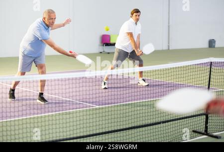 Älterer Mann spielt Pickleball im Team mit männlichem Partner im Haus Stockfoto