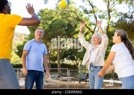 Alte multinationale Menschen spielen Volleyball-Aktivität auf einem Sommerspielplatz für Sport im Frühling draußen Stockfoto