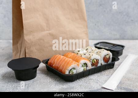 Plastikteller mit leckeren Sushi-Rollen, Essstäbchen und Papiertüte auf hellem Grunge-Hintergrund. Lieferkonzept Stockfoto