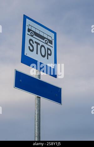 Eine vertikale Aufnahme eines blauen Bushalteschilds mit einem leeren Zielschild darunter. Das Schild zeigt ein schwarzes Bussymbol und das Wort „STOP“ in weiß. Stockfoto