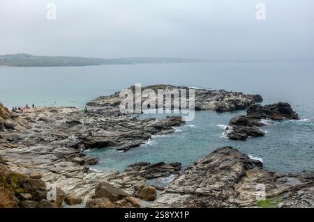Besucher genießen die felsige Küste am Godrevy Point mit Wellen, die sanft gegen die Klippen unter grauem Himmel in Cornwall, England, krachen Stockfoto
