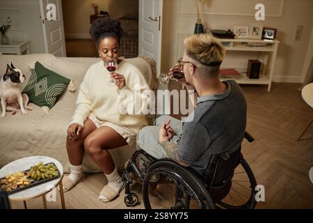 Hochwinkelaufnahme eines multiethnischen Paares, das köstliche Rotwein verkostet, bei einem romantischen Date in einem gemütlichen Wohnzimmer, während Sie den Moment zusammen genießen Stockfoto