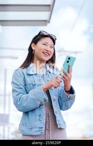 Lächelnde junge Frau, die Smartphone in der städtischen Umgebung hält. Vertikal Stockfoto