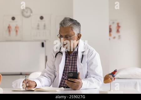Reifer männlicher Arzt benutzen Telefon am Schreibtisch im Krankenhausbüro Stockfoto