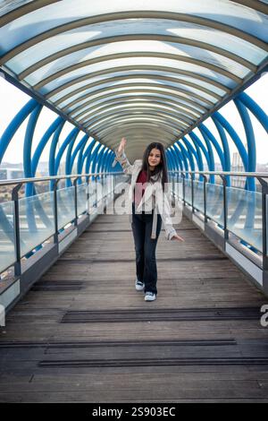 Stilvolle junge Frau, die auf einer modernen Fußgängerbrücke winkt Stockfoto