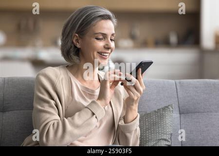 Entspannte, glückliche, reife Frau, die mit der Handy-App auf der Couch interagiert Stockfoto