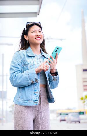 Lächelnde junge Frau, die Smartphone in der städtischen Umgebung hält. Vertikal Stockfoto