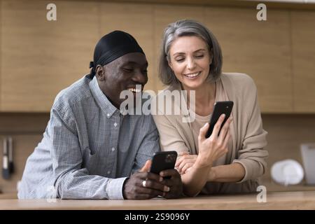 Freundliche, multiethnische Paare mittleren Alters teilen Informationen zwischen zwei Smartphones Stockfoto