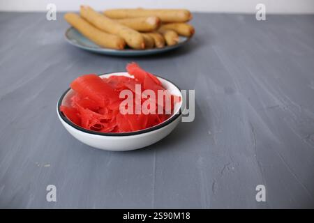 Roter marinierter Ingwer auf einem Teller auf grauem Hintergrund, Nahaufnahme des Seitenwinkels. Das Konzept der würzigen fermentierten Lebensmittel. Stockfoto