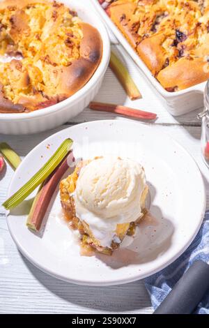Süße Rhabarberbeerkuchen, selbstgemachter Schwammkuchen mit Rhabarber und Erdbeere, serviert mit Vanille-Eiskugel, auf sonnigen weißen Holzkrem Stockfoto