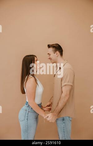 Lächelndes Paar, das zusammen vor einem beigefarbenen Studio-Hintergrund steht Stockfoto
