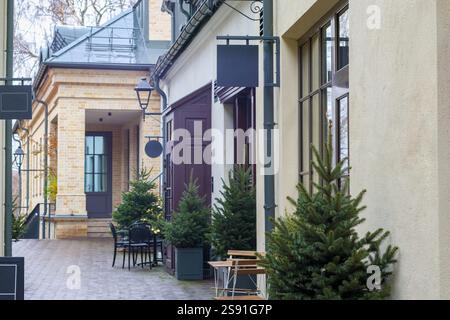 Ein schmaler Abschnitt der Straße mit einer Holzterrasse, auf der Weihnachtsbäume in Töpfen wachsen und es gibt kleine Tische mit Stühlen. Stockfoto