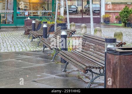An empty square with several wooden benches lined up along a paved sidewalk. Stockfoto