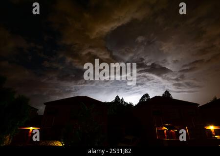 Blechbeleuchtung in Wolken hinter den Dächern städtischer Wohnhäuser. Die Natur erleuchtet den städtischen Himmel. Stockfoto