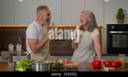Lustiges weißes Paar verliebt reife ältere ältere ältere Frau mittleren Alters und Ehemann im Ruhestand verheiratete Familie sang fröhlich bei Löffeln Küchengeschirr Stockfoto