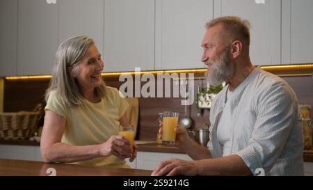 Kaukasisches Ehepaar glücklicher Rentner Mann der Familie, der mit der reiferen Frau spricht, Frau in der Küche lachend männlich weiblich, die Orangensaft trinkt Stockfoto