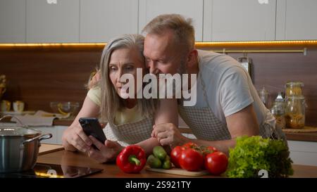 Kaukasisches verheiratetes Paar, das Familie verbindet, alter reifer Frau Mann las Kochrezept auf Handy älterer 50er Mann Ehemann redet umarmt Einkaufen Stockfoto