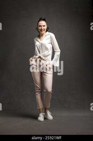Portraet in voller Laenge von laechelnden stilvolle Frau posiert ueber grauen Hintergrund Stockfoto