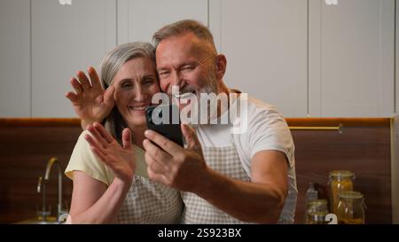 Reifes Ruhestand kaukasisches Paar Familie alte glückliche Großeltern sprechen online Videoanruf mit Handy zu Hause Küche lächelnde ältere Frau Stockfoto