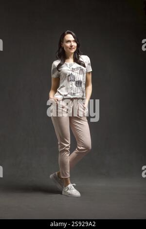 Portraet in voller Laenge von laechelnden stilvolle Frau posiert ueber grauen Hintergrund Stockfoto