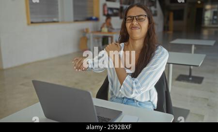 Frau, die im Büro arbeitet, hat Schulterschmerzen, während sie mit einem Laptop an ihrem Schreibtisch sitzt Stockfoto