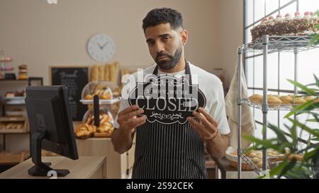 Hübscher Mann, der ein Schild in der Bäckerei hält, mit verschiedenen Backwaren und Kuchen Stockfoto