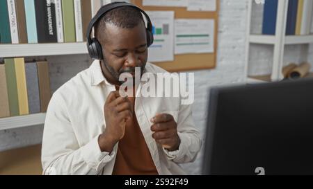 Junger Mann tanzt fröhlich mit Kopfhörern in einer modernen Büroumgebung, die Freude und Energie in professioneller Arbeitsplatzeinrichtung und stilvoller Inneneinrichtung ausstrahlt Stockfoto
