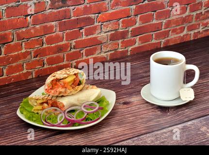 Saftige Fleisch-Shawarma auf einem Salatblatt mit roten Zwiebelringen und einer Tasse heißem Tee auf einem Holztisch. Nahaufnahme. Stockfoto