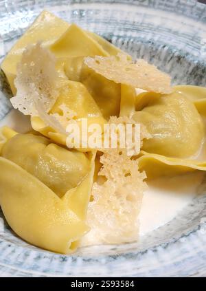 Nahaufnahme mit frischem Spinat und Ricotta-Tortelloni, garniert mit cremiger Sauce und knusprigen Parmesanflocken für ein verführerisches Gericht Stockfoto