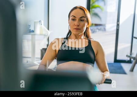 Eine Frau trainiert auf einem Rudergerät im Fitnessstudio, Porträt ihres Gesichts fokussiert Stockfoto