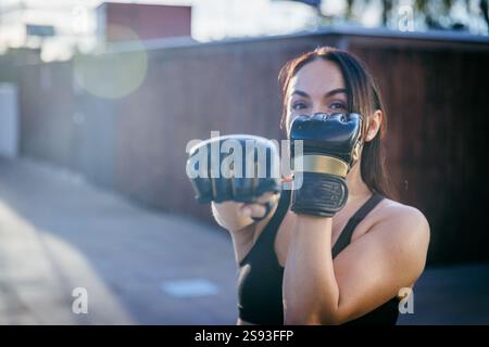Eine Frau in einem schwarzen Tanktop boxt mit Handschuhen. Sie trägt einen schwarzen Handschuh auf der linken Hand und einen schwarzen Handschuh auf der rechten Hand Stockfoto