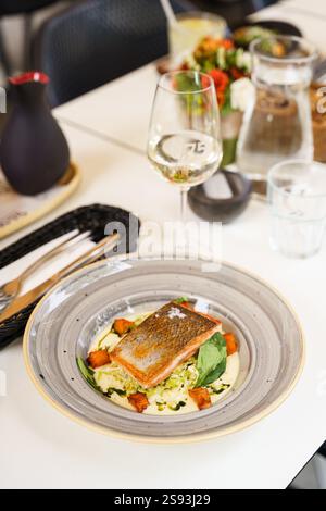 Ein perfekt gegrilltes Lachsfilet, serviert mit geröstetem Gemüse und einer cremigen Sauce auf einem dekorativen Teller. Das Gericht wird mit Spinatblättern garniert. Stockfoto