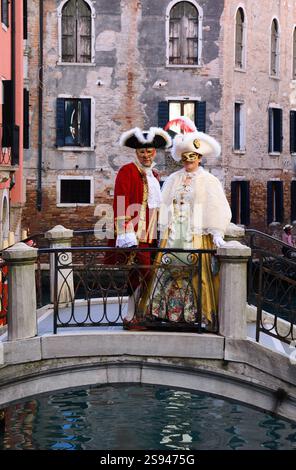 VENEDIG, ITALIEN - 16. FEBRUAR 2015: Unbekanntes Paar mittleren Alters in traditionellen Karnevalskostümen auf einer kleinen Brücke über den Kanal. Der Karneval in Venedig. Stockfoto
