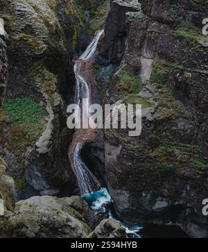 Moosbedeckter Mogafoss-Wasserfall, der durch zerklüftete Klippen in Südisland kaskadiert. Stockfoto