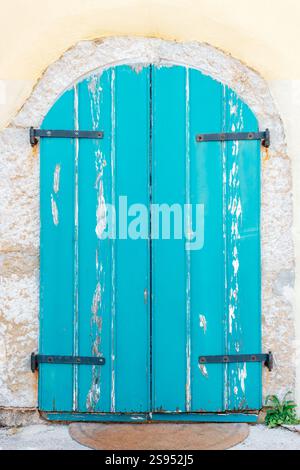 Alte türkisfarbene Holztür mit abblätternder Farbe und Steinrahmen, die den mediterranen Stil repräsentiert. Stockfoto