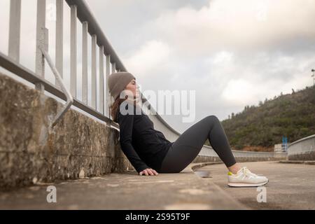 Läuferin, die nach dem Joggen erschöpft auf der Straße sitzt Stockfoto