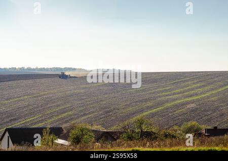 Der Traktor pflügt das Feld, hebt Staub auf und wendet schwarzen Boden auf dem Land. Landwirtschaft, Frühjahrsfeldarbeit Stockfoto